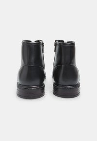 Botas de cuero negro hasta el tobillo con un acabado suave, cremalleras laterales y un tacón bloco texturizado en marrón oscuro. Diseño de punta redonda.