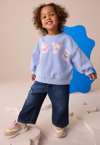 Hellblaues Sweatshirt mit Cartoon-Grafik, lässige dunkelblaue Jeanshose und beigen Sneakern mit pastellfarbenen Akzenten. Glatte Textur, entspannter Stil.