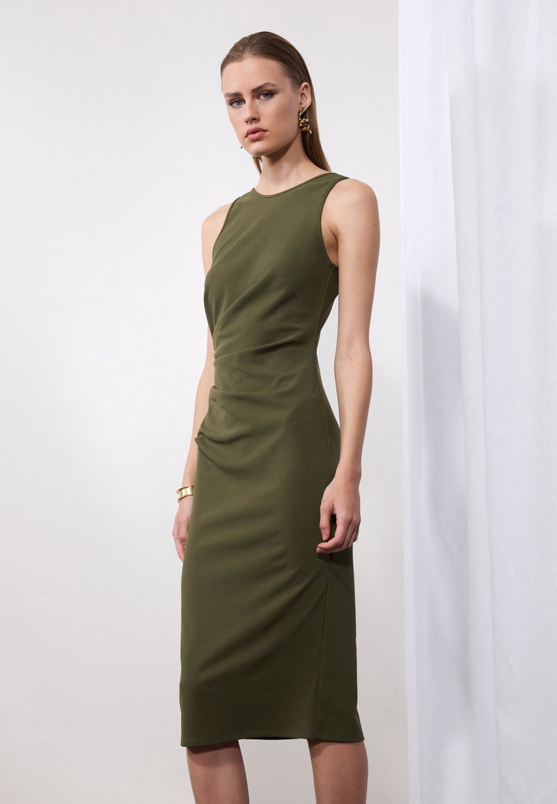 Rochie verde măsliniu, ajustată, cu design fără mâneci, textură drapată și tăietură până la genunchi. Accentele includ un detaliu subtil și o țesătură netedă.