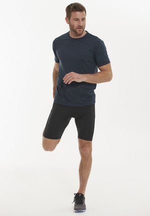 Blå atletisk T-shirt med korte ærmer, parret med sorte kompressionsshorts med et logo på siden. Sorte løbesko fuldender outfittet.