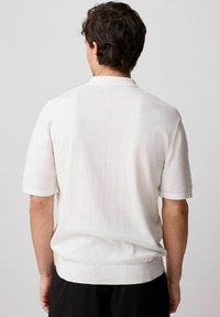 Polo de punto de manga corta blanco con una textura suave, cuello y puños acanalados. Corte casual con un diseño de espalda sin costuras.