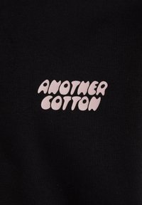 Material textil din bumbac negru cu un text alb care citește "ANOTHER COTTON" într-un font rotunjit și jucăuș.
