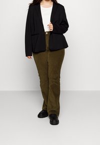 Sort blazer med struktureret design, parret med olivengrøn corduroy-bukser. Sorte sko fuldender outfitet.