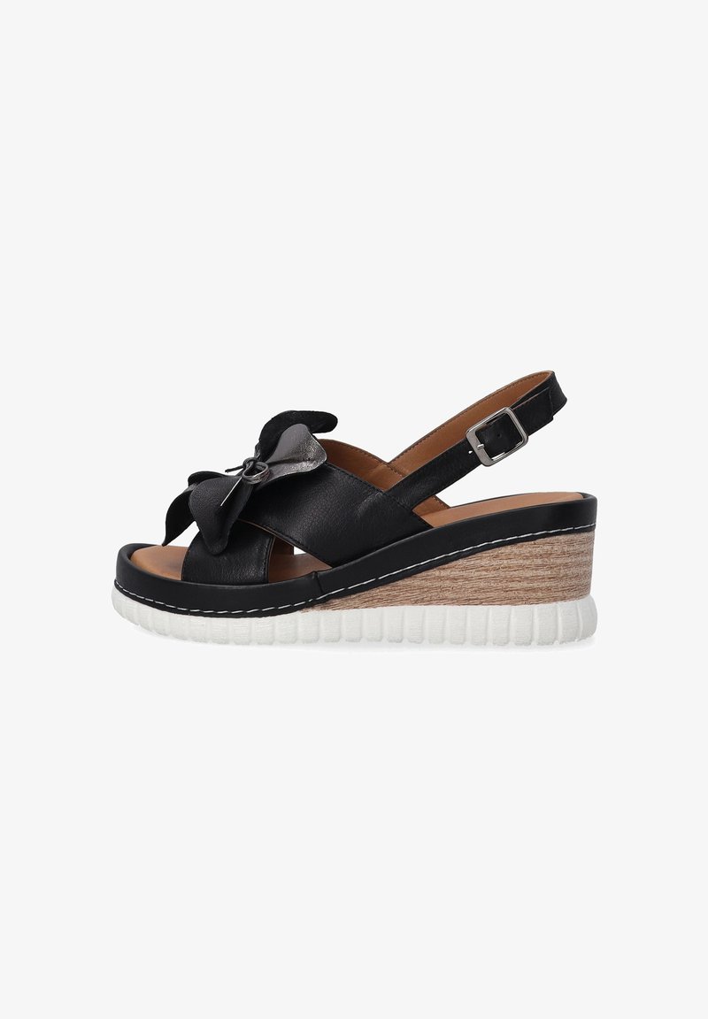 Černé kožené sandály na klínu s dekorativní mašlí a nastavitelným pásem kolem kotníku. Vlastnosti zahrnují texturovanou bílou platformu a dřevěný klínový podpatek.