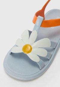 Blå plast sandaler med en oransje stropp og hvit tusenfryd dekorasjon med en gul sentrum. Teksture såle med en rillekant.