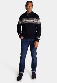 Marineblauw gebreid sweatshirt met een ronde hals en een knoopsluiting met drie knopen; heeft een witte en grijze gestreepte band over de borst. Gecombineerd met donkere jeans.