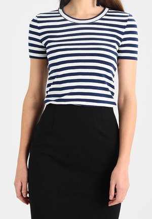 Frau trägt ein marineblau-weiß gestreiftes kurzärmeliges Shirt, das in einen hoch taillierten schwarzen Rock gesteckt ist, abgebildet von den Schultern bis zur Hüfte.