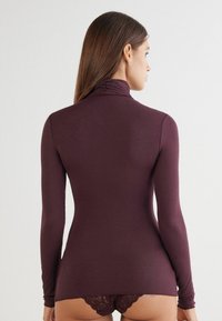 Vínová dlouhá rukávová roláková blůza s přiléhavým střihem, měkkou texture a nařasením u krku, doplněná o spodní prádlo s krajkovým lemem.