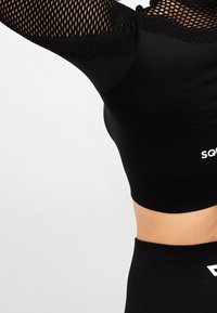 Schwarzes sportliches Crop-Top mit Mesh-Ärmeln, das ein figurbetontes Design aufweist und ein kontrastierendes weißes Logo am Saum hat. Glatter Stoff mit dehnbarem Material.