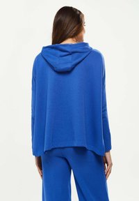 Blue hooded pullover, oversized fit, textured fabric, long sleeves, dropped shoulders. Paired with matching blue pants, casual style.