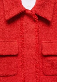 Red textured jacket with a collar, featuring two front pockets and frayed detailing along the center seam. Material appears soft and woven.