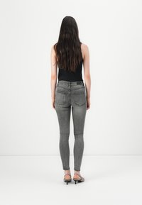 Gray skinny jeans with a faded wash, featuring back pockets and a smooth texture, paired with a black tank top and heeled sandals.