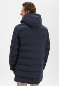 Donkerblauwe gewatteerde jas met een hoge kraag, capuchon en horizontaal doorgestikt ontwerp. Heeft een gladde textuur en een strakke pasvorm.