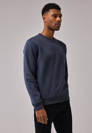 Mørkeblå crewneck sweatshirt i blødt materiale med ribbede manchetter og kant. Har et lille, trykt logo på forsiden.