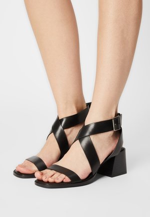Zwarte leren sandalen met kruisende banden en een verstelbare gesp. Blokhakontwerp met een soepele afwerking en open teen.