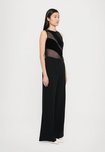 Black sleeveless top with sheer panel details paired with high-waisted, wide-leg black trousers. Smooth fabric with a refined finish.