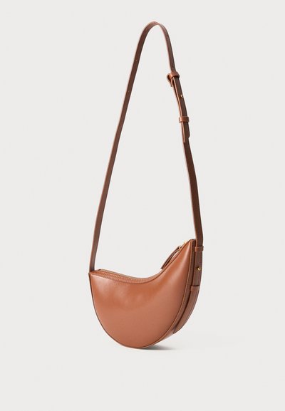 Bolsa de ombro em forma de crescente, em pele castanha, com alça ajustável e fecho dourado, sobre fundo branco.