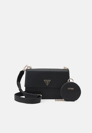 Czarna torebka Guess typu crossbody ze złotym logo na klapie, dołączona pasująca okrągła portmonetka oraz regulowany pasek, na gładkim tle.