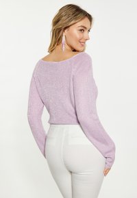 Helllila gestrickter Pullover mit lockerer Passform und langen Ärmeln. Verfügt über einen dezenten metallischen Glanz. Kombiniert mit weißen, taillierten Hosen.