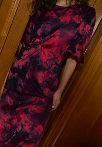 Šaty s květinovým vzorem v tmavě fialové a červené barvě, se zvýrazněným pasem a krátkými nafouklými rukávy. Hladká látka a design sahající ke kolenům.