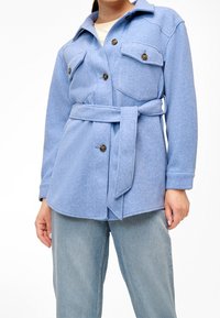 Modrá, plstěná košile-jacket s páskem v pase, s dvěma náprsními kapsami a velkými knoflíky. Nosit na světlých modrých džínách.