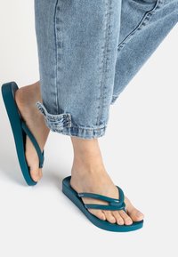 Türkise Flip-Flops mit dicker Sohle und doppeltem Riemendesign. Tragen Sie sie zu hochgekrempelten hellblauen Jeans für einen lässigen Look.