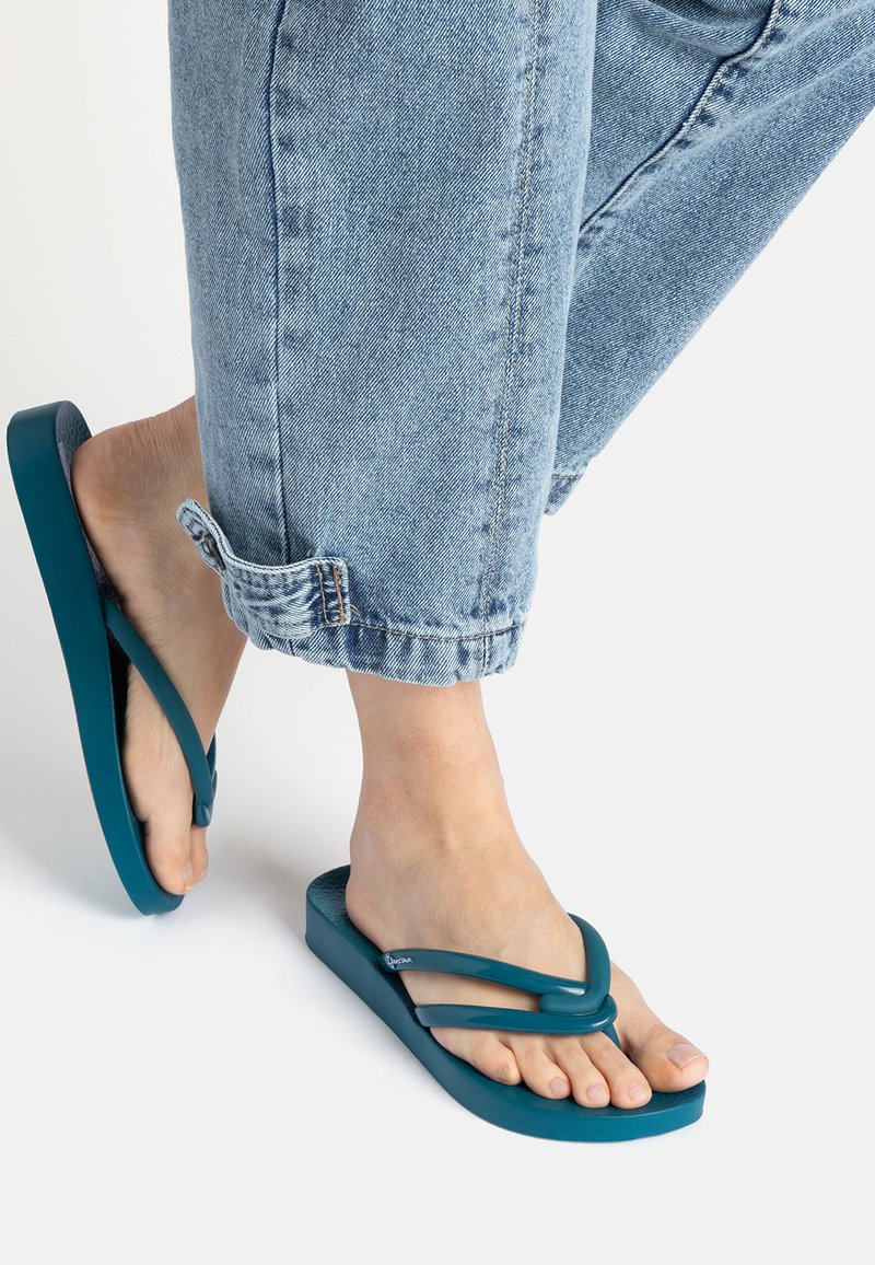Türkise Flip-Flops mit dicker Sohle und doppeltem Riemendesign. Tragen Sie sie zu hochgekrempelten hellblauen Jeans für einen lässigen Look.