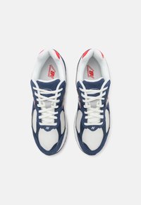 Paire de baskets New Balance bleu marine et blanc avec des lacets blancs, tissu en mesh et accents rouges, vues de dessus sur fond blanc.