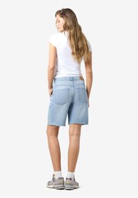 Shorts in denim blu chiaro con orlo scucito, caratterizzati da un taglio classico e due tasche posteriori. Abbinati a una camicia bianca a maniche corte e scarpe da ginnastica.