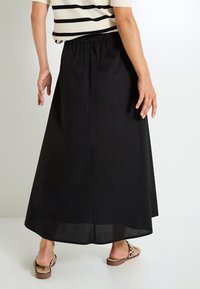 Falda maxi negra con cinturilla elástica, textura suave y dobladillo hasta el tobillo, combinada con sandalias de estampado animal para aportar contraste.