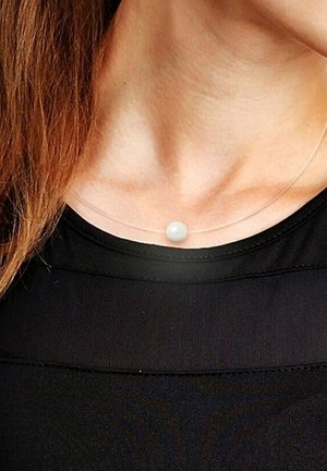 Collier transparent avec un pendentif en perle blanche, porté sur un cou nu, au-dessus d'un haut noir. Le collier a un design simple et minimaliste.