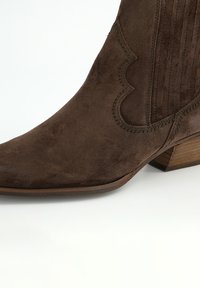 Botín de ante marrón con puntera puntiaguda, detalles cosidos y tacón de bloque de madera, con paneles acanalados a lo largo de los laterales.