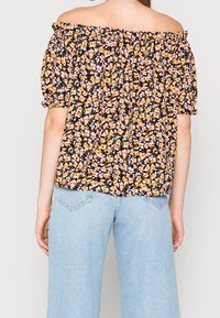 Blouse à épaules dénudées avec un fond noir orné d'un motif floral rose et jaune. Manches élastiquées et coupe ample.