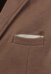 Blazer in maglia marrone con taschino sul petto dotato di una fodera interna di colore chiaro e tessuto texturizzato. Il design è sagomato con un colletto a scollo.