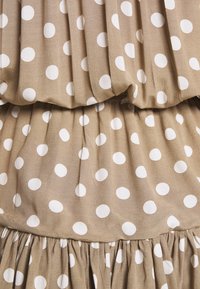 Beige fabric with white polka dots, featuring gathered and pleated texture in horizontal layers.