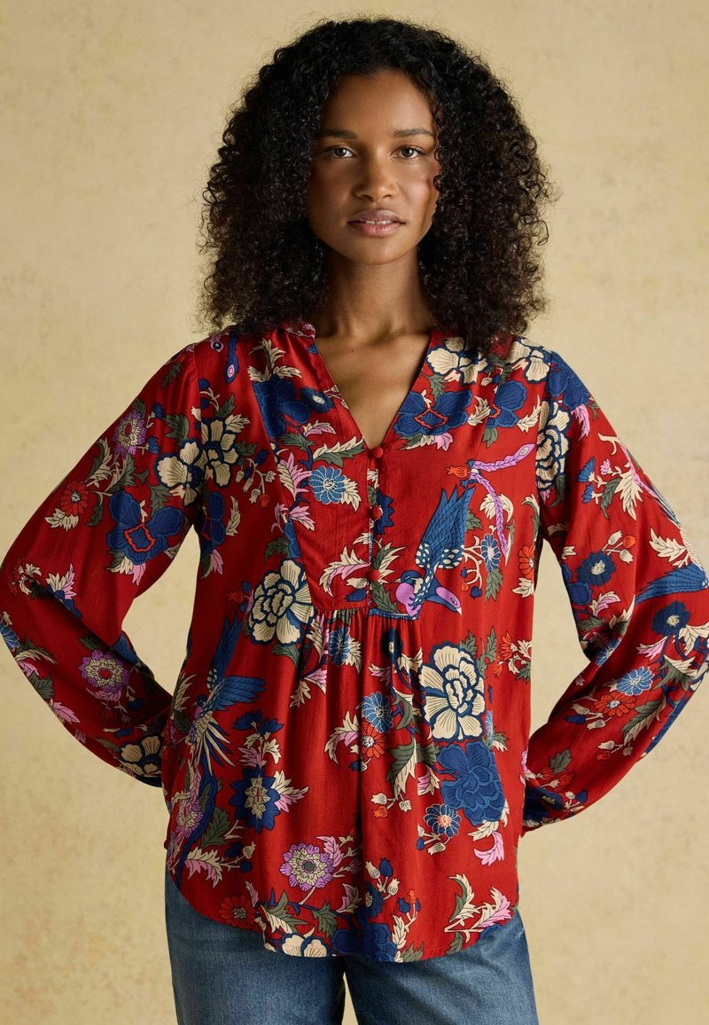 Rote Bluse mit langen Ärmeln, V-Ausschnitt, Knopfdetails und einem fließenden Schnitt. Blumen in Blau, Rosa und Creme.
