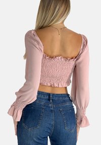 Rosa cropped Top mit Puffärmeln, gerafftem Oberteil und rüschengesäumtem Saum. Getragen mit dunkelblauen Jeans aus Denim mit Gesäßtaschen.