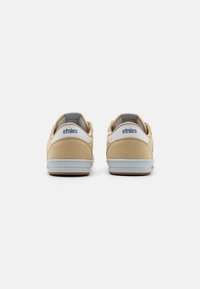 Beige suede sneakers with white leather accents and light blue soles, featuring a padded collar and "etnies" logo on the back.