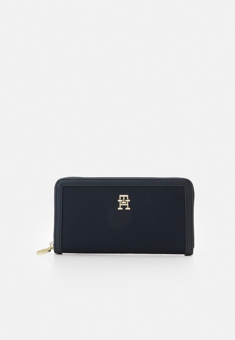 Portafoglio in tessuto blu navy con hardware dorato, caratterizzato da un logo in rilievo molto evidente. Forma rettangolare con chiusura a cerniera e superficie liscia.