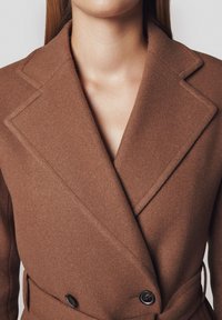 Brązowy płaszcz z mieszanki wełny z podwójnym zapięciem, ostrymi klapami, teksturowanym materiałem i wiązanym w pasie, z dwoma czarnymi guzikami.