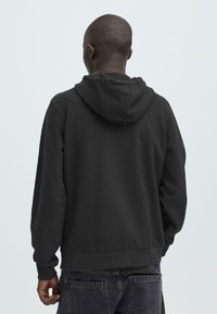 Zwarte hoodie van een gestructureerde stof, met capuchon en aantrekkoord en geribbelde manchetten. De achterkant heeft een eenvoudig, strak ontwerp zonder afbeeldingen.