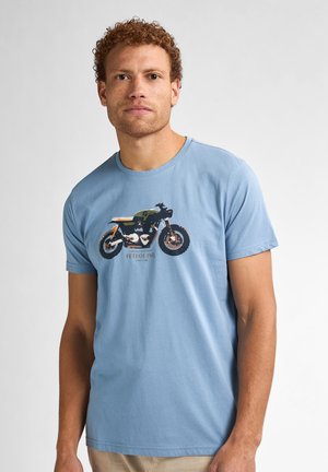 Lichtblauw katoenen T-shirt met een motorgrafiek in zwart en oranje, met de tekst "PETROL IND. SINCE 1990" onder het ontwerp.