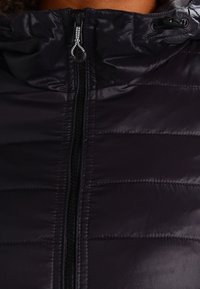 Chaqueta negra tipo puff con cierre frontal, diseño acolchado texturizado y capucha ajustable con cordones. Tejido suave y brillante.