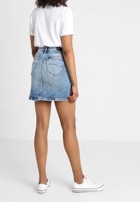 Džínová áčková sukně světle modré barvy s třepeným lemem, dvěma zadními kapsami, doplněná bílým tričkem a bílými teniskami.