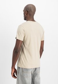 Beesi lühikeste varrukatega T-särk, mis on valmistatud pehmest puuvillast, ümarate kaelustega ja mugava lõikega, kombineeritud heledate hallide teksadega.