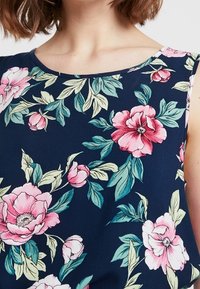 Kukkakuvioinen olkaimeton toppi tummansinisellä taustalla, jossa on vaaleanpunaisia ja vihreitä kukkakuviota sekä lehtiä. Kevyt, sileä kangastekstuuri.