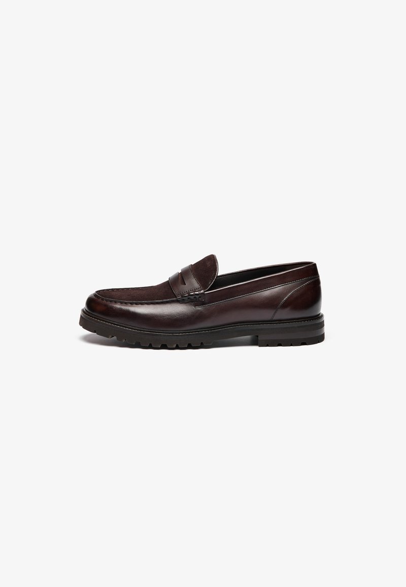 Mocassins de couro castanho com um detalhe em camurça, bico redondo e sola de borracha texturizada. Apresentam costuras decorativas e um pequeno tacão.