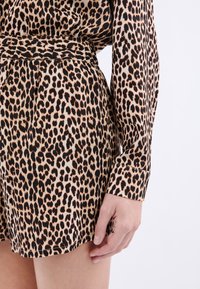 Luipaardprint jurk met een getailleerde taille, lange mouwen en een zijdezachte textuur. Kenmerkt zich door een mix van tan, zwart en roestkleurige vlekken.