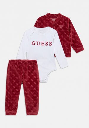 Ensemble de vêtements pour bébé trois pièces avec body blanc à manches longues imprimé "GUESS,", veste rouge à motifs et pantalon rouge assorti.
