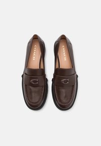 Brown leather loafers with a round toe, featuring a stitched detail and a raised logo on the band. Black rubber sole with a textured finish.